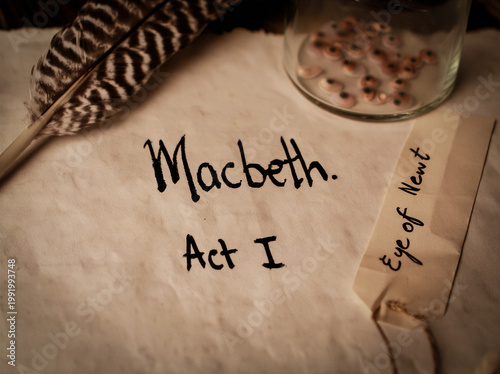the words written with quill Macbeth and Act I onto parchment, a feather quill lays to the side and a small thin glass bottle filled with small newt eyes authentic scene