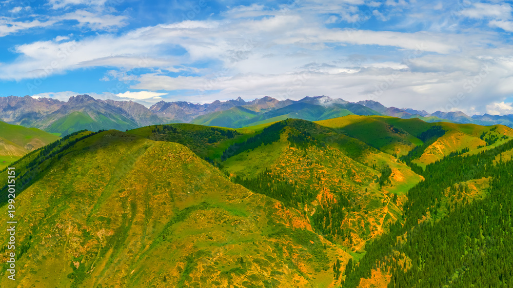 Obraz premium Expansive green hills with distant mountains under cloudy sky