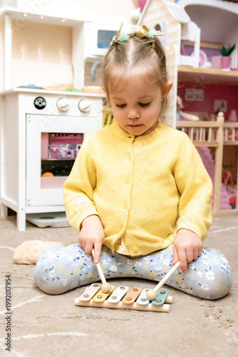 Toddler girl xylophone focused playing floor dollhouse wide shot