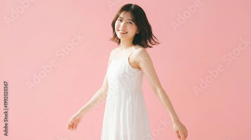 Cheerful Japanese woman in a white dress walking and smiling on pink background