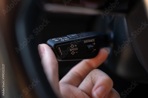 Konstfotografi Close-up of hand using cruise control stalk in modern car, showing speed setting and distance adjustment controls on steering column lever