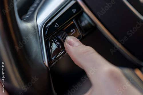 Photography Close-up of finger using steering wheel control buttons and scroll wheel in modern car, showing multifunction interface for driver settings