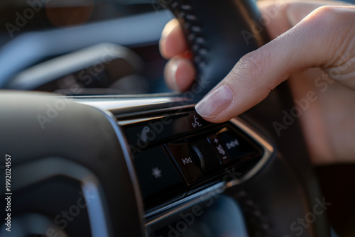 Bilde på lerret Close-up of finger pressing voice command button on steering wheel in modern car, with phone and audio controls on multifunction panel
