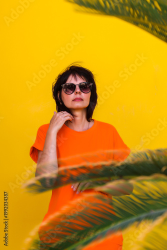 portrait of a woman in orange clothing against a yellow house wall, framed by palm branches, radiating a relaxed atmosphere.