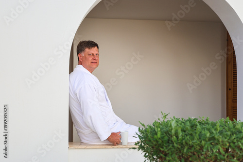 A man vacation sits in a robe and drinks coffee.