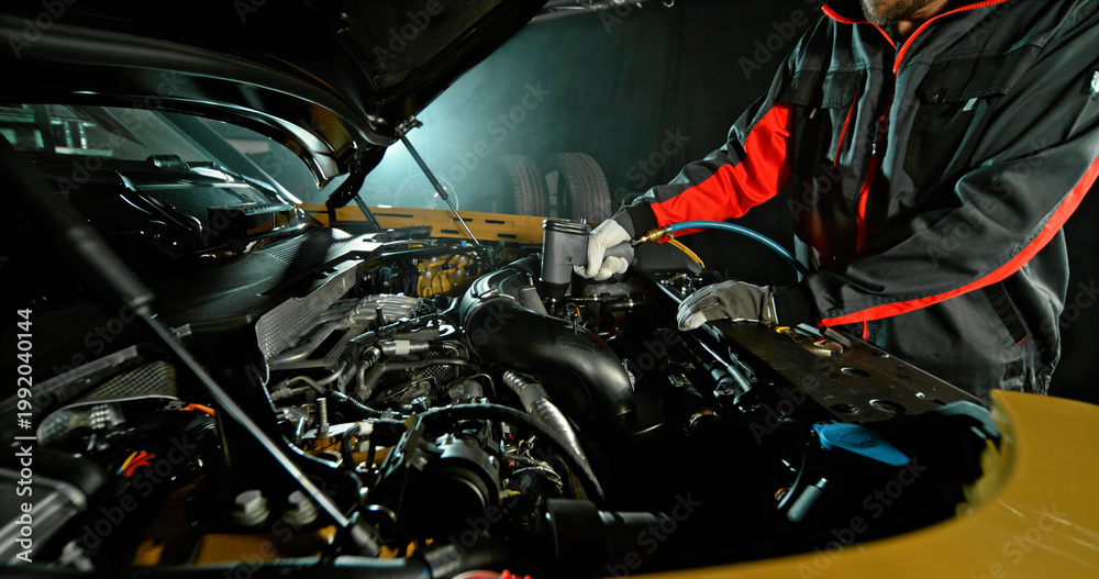 Fototapeta premium Mechanic repairing car engine in workshop, using tools with dramatic lighting. Automotive maintenance and professional service concept.