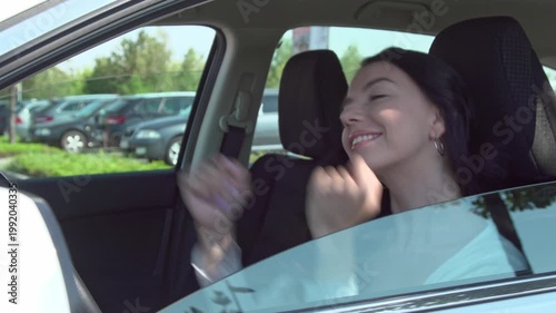 Happy young woman dancing and listening to music inside a car. cheerful woman with long dark hair smiles and moves her hands to the beat of music while sitting in the driver's seat