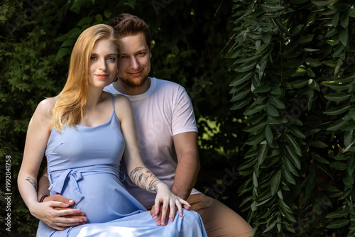 Pregnant young woman  and her husband are posing at the gardden. Horizontally. 