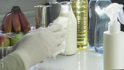 Disinfecting groceries with spray sanitizer during pandemic. Various food containers, including water bottles and oil, sit on a white table awaiting sanitization to ensure safety and hygiene.