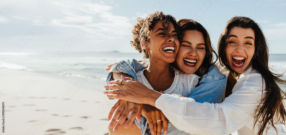 Obraz premium Three friends laughing and hugging together on a bright sunny beach