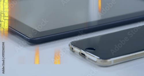 Resting smartphone in clear case showing home button on glossy desk, tablet reflections, copy space