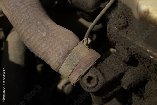 A detailed, macro-style photograph of a vehicle's engine bay, showing various dusty components including wires, hoses, and mechanical parts