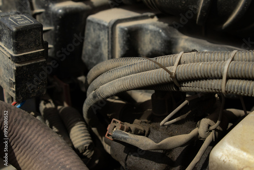 A detailed, macro-style photograph of a vehicle's engine bay, showing various dusty components including wires, hoses, and mechanical parts