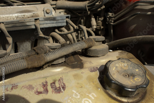 A detailed, macro-style photograph of a vehicle's engine bay, showing various dusty components including wires, hoses, and mechanical parts
