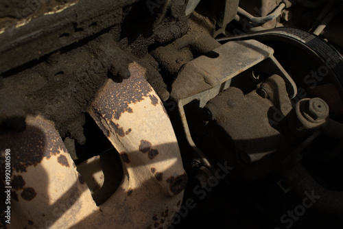 A detailed, macro-style photograph of a vehicle's engine bay, showing various dusty components including wires, hoses, and mechanical parts