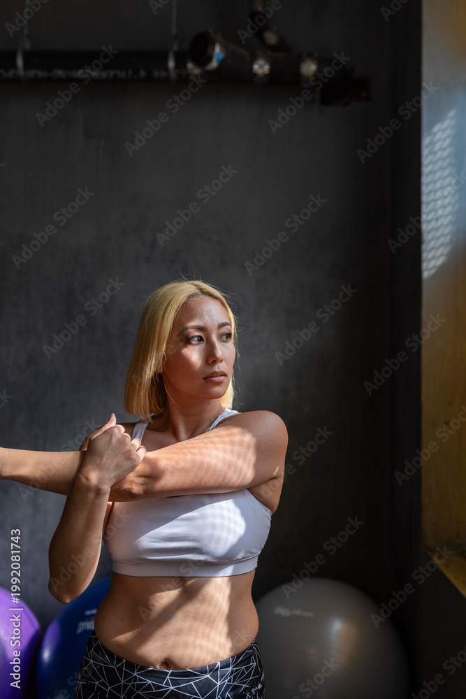 Obraz premium Woman stretching in gym sunlight.