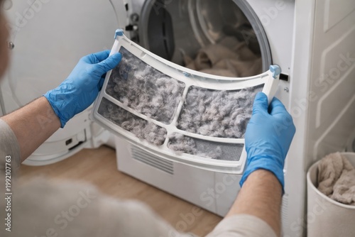 Cleaning Dryer Lint Filter Before Every Load. Hands wearing gloves remove a clogged dryer lint screen, showing routine appliance maintenance for safety, airflow, and better energy efficiency.