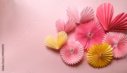 Close-up of bunch of origami paper pink and yellow daisies and pink heart origami on pale pink table on pale pink background with copy space
