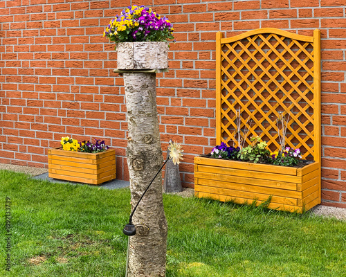Creative garden decor features a birch log planter topped with colorful pansies next to a wooden flower box and trellis