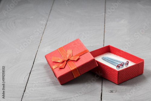 Red gift box revealing three metal screws, thoughtful gift for DIY and construction