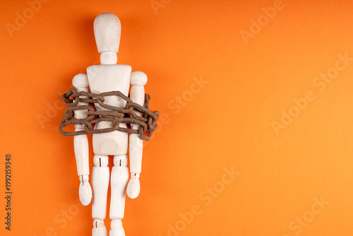 Wooden mannequin bound with chain on orange surface, captivity and powerlessness concept