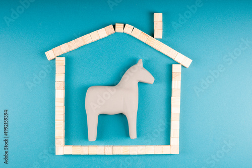 Toy horse trapped inside picture frame shaped as house, domestic limitation and security theme