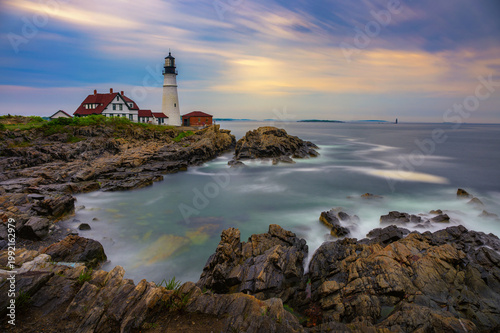 Sunset view of Portland Head Lighthouse overlooking rocky shoreline and calm ocean waters in Cape Elizabeth, Maine, USA. Long exposure.