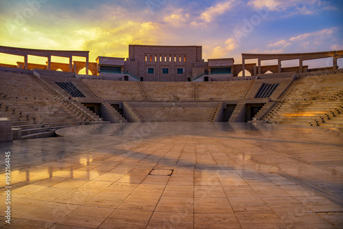 Katara Amphitheatre in Katara Cultural Village with symmetrical stone seating and central stage under a colorful sunset sky in Doha, Qatar.