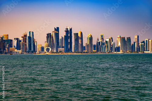 Modern skyscrapers of West Bay financial district in Doha at sunset seen across Doha Bay from the Corniche promenade with colorful gradient sky, Qatar