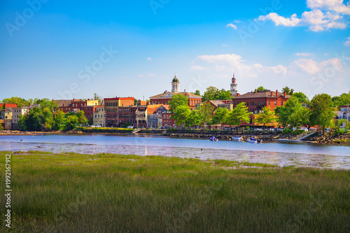 Historic buildings and church steeples of Exeter, New Hampshire, viewed across the Squamscott River on a clear summer day.