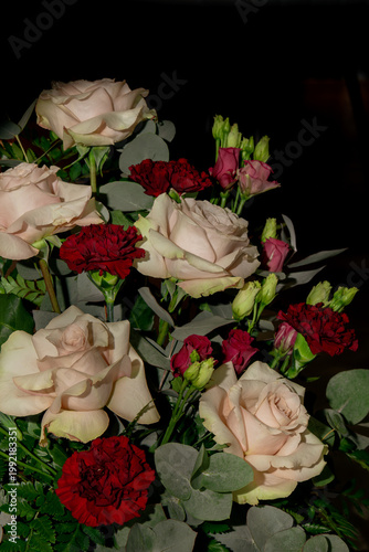 Elegant bouquet of cream roses and red carnations with greenery on a dark background, softly lit to create a romantic, moody, and luxurious atmosphere.