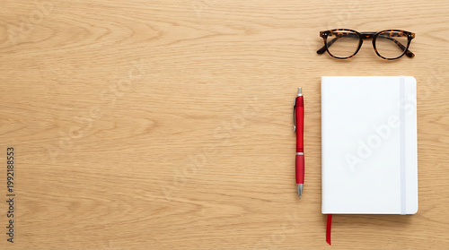 White journal with red pen and glasses on wooden desk copy space