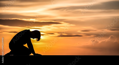 Silhouette of a person kneeling in prayer during a beautiful sunset with clouds