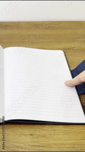 A close-up video, filmed vertically, showing a blue notebook being unpacked on a table.