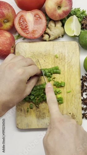 Vertical close-up video of chopping fresh green onions on a wooden cutting board.