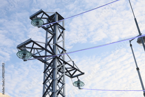 Metal tower holds high-voltage cables against a blue sky