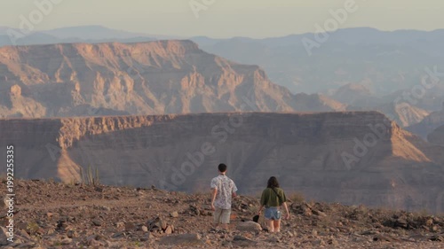 Young European couple walk across desert landscape, Fish River Canyon visible behind