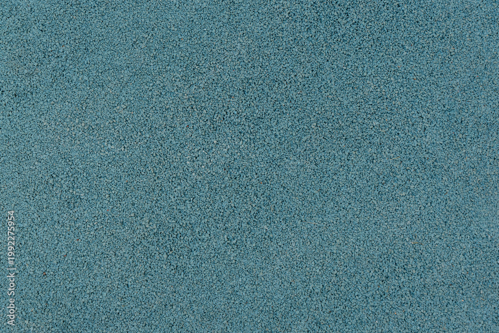 Fototapeta premium Blue rubber crumb surface texture from a sports or playground area, photographed full frame as a granular background with fine detail. Abstract turquoise textured background.