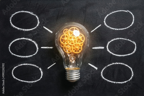 Conceptual light bulb with golden gears inside on blackboard with chalk mind map circles.