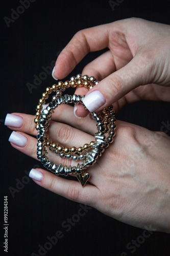 Hand holding trio of metallic bead bracelets with gold heart charm, dark background