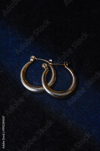 Pair of sleek gold hoop earrings on dark fabric background, minimalist style