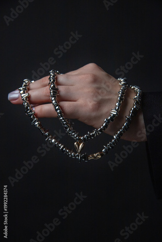 Hand showcasing silver chain with gold element, stark dark background