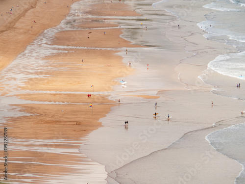 Billede på lærred Sunny beach day in Zarautz with surfers and sunbathers enjoying the waves