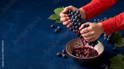 Woman squeezing fresh purple grape with hand into bowl. Culinary process of making juice and jam. Concept of homemade winery, organic healthy food preparation and harvest season cooking.