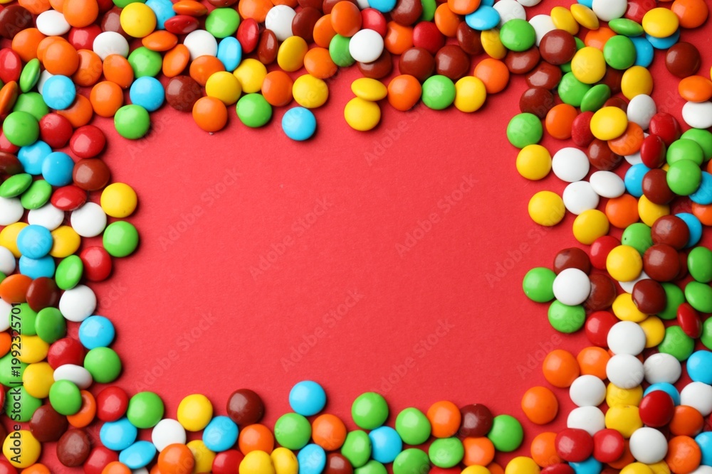 Obraz premium Frame made of delicious colorful candies on red background, top view. Space for text