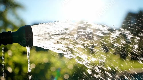 Water spraying from a garden hose nozzle in bright sunlight. Clear droplets sparkling and glistening in slow motion. Refreshing outdoor watering