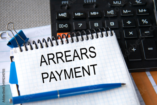 Notebook with the words ARREARS PAYMENT in the notebook on the background of a black calculator