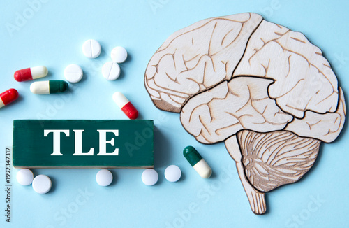 On a blue background with a model of a brain lies a wooden block with the acronym TLE