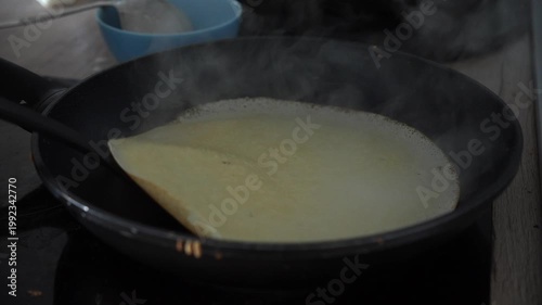 Pancake flipped in frying pan during indoor breakfast cooking.