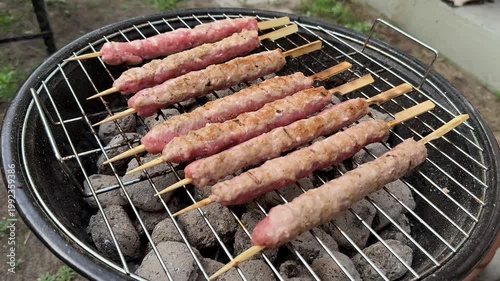 Skewered minced meat kebabs grilling over charcoal on a round barbecue, outdoor backyard cooking scene with smoky heat and casual summer gathering mood